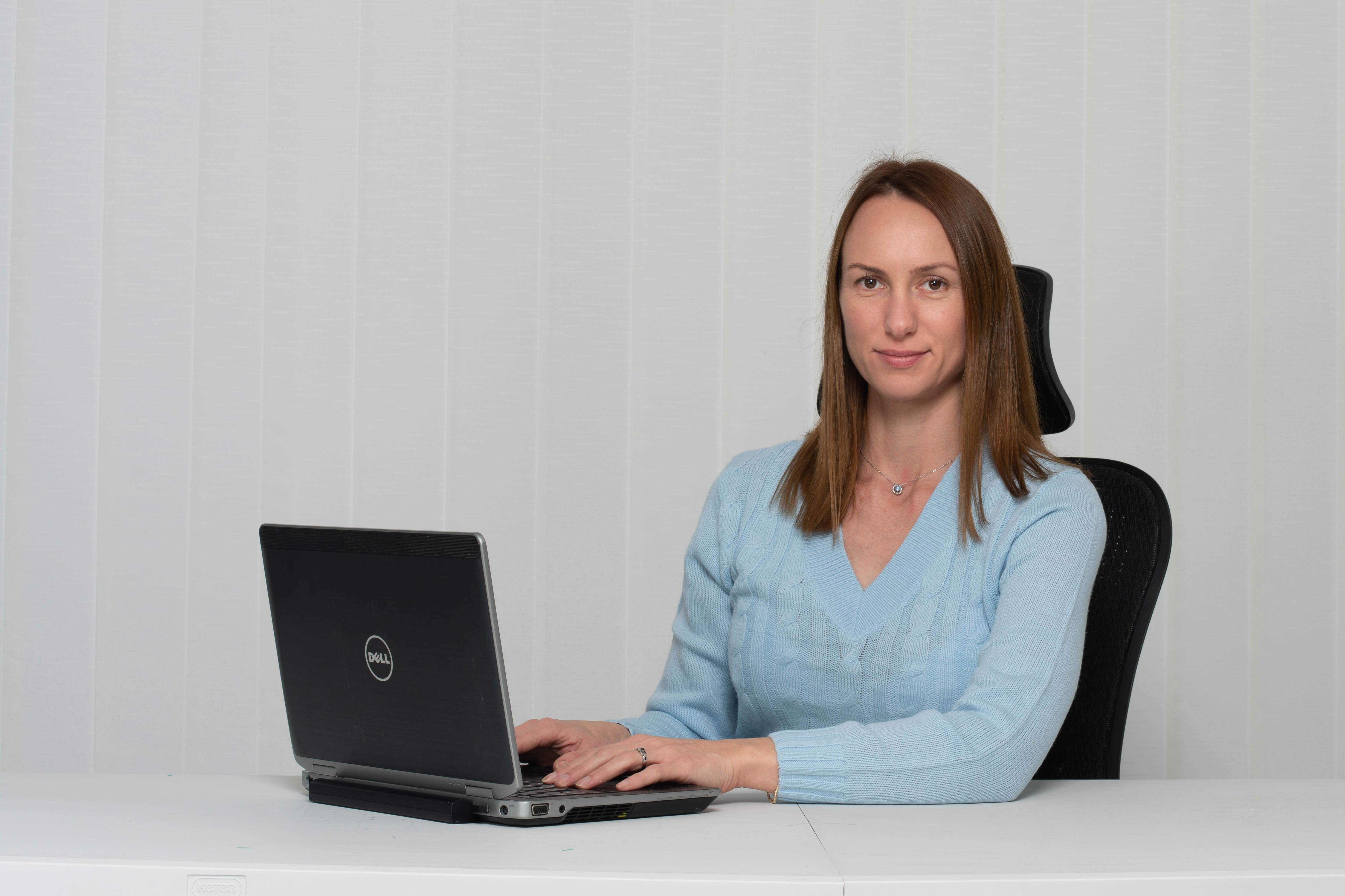 בחורה עם חולצה כחולה יושבת עם ידיים על השולחן על הנייד מחייכת למצלמה