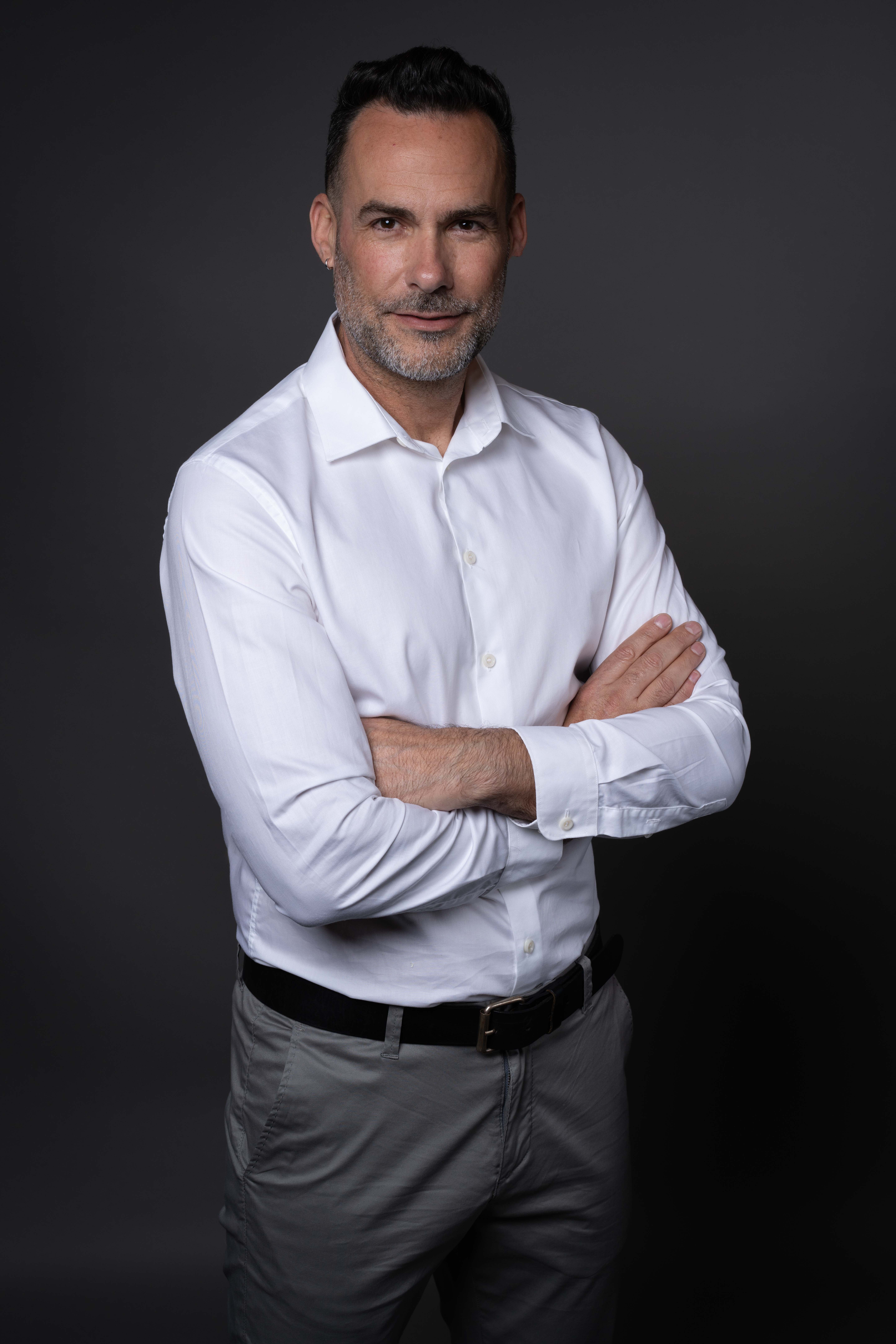 גבר עם חולצה לבנה משלב ידיים על רקע כהה