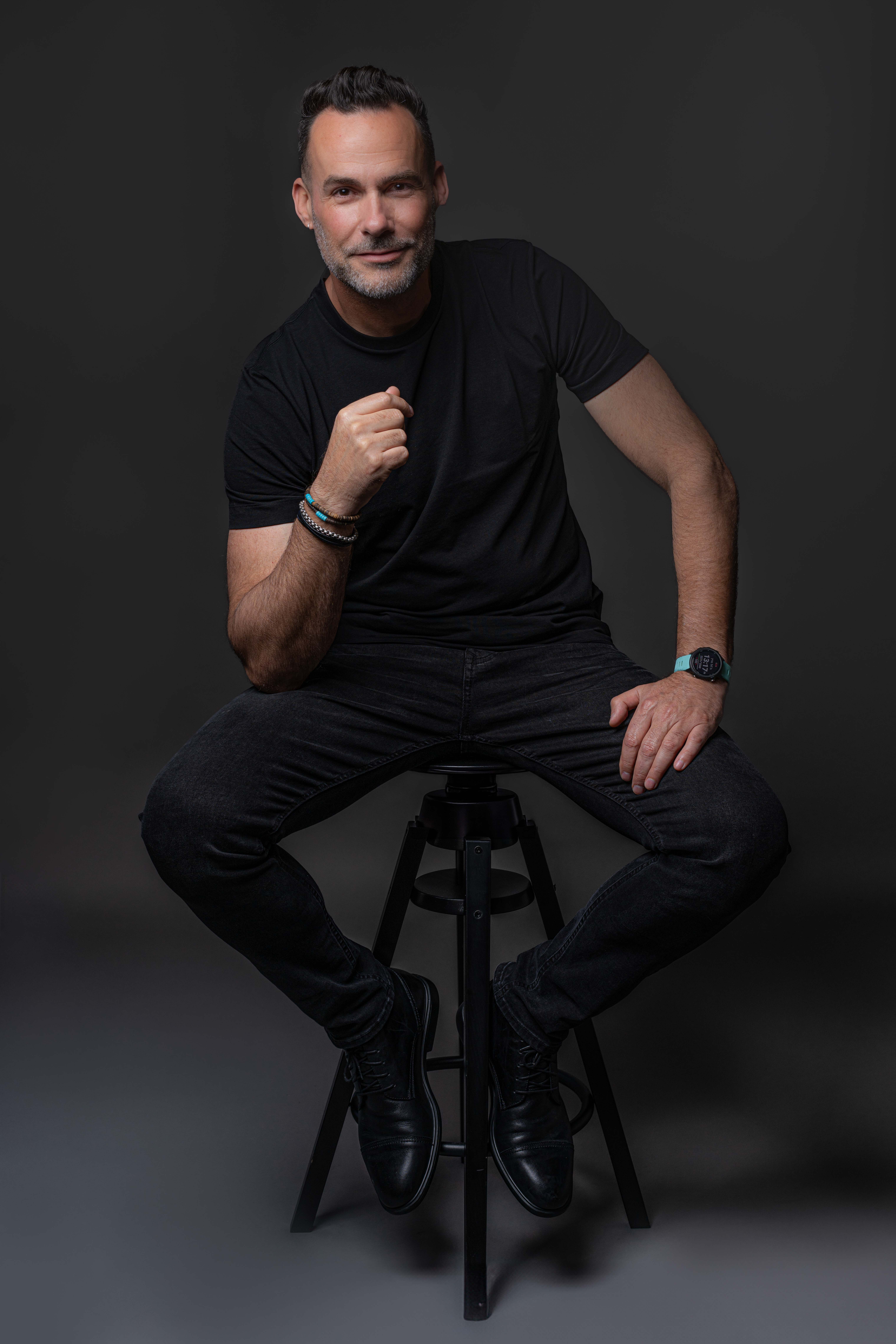 גבר יושב על כיסא בבגדים כהים על רקע כהה